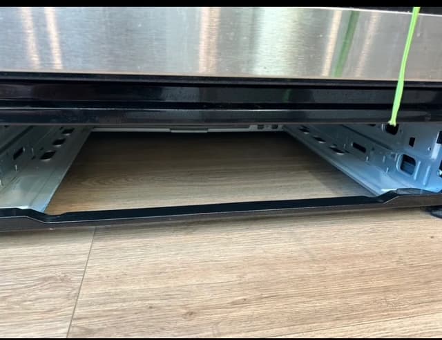 Empty bottom compartment of a stainless steel oven showing metal rails and wood-look flooring.