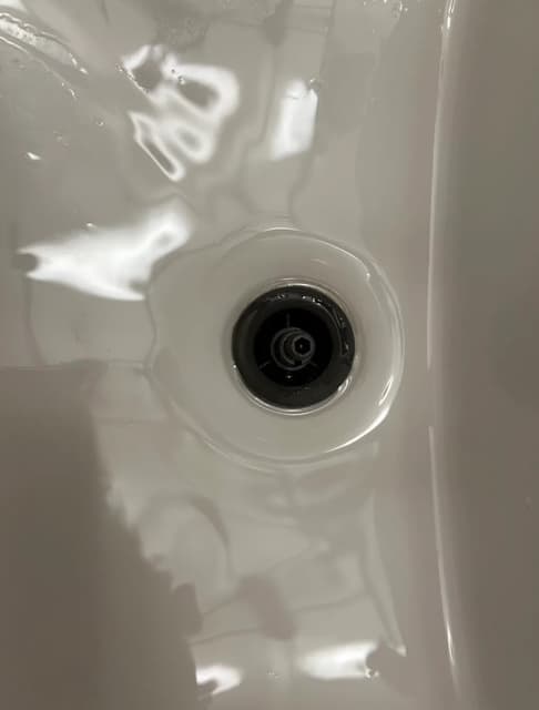 Overhead view of a white ceramic sink basin with water reflecting around a dark drain.
