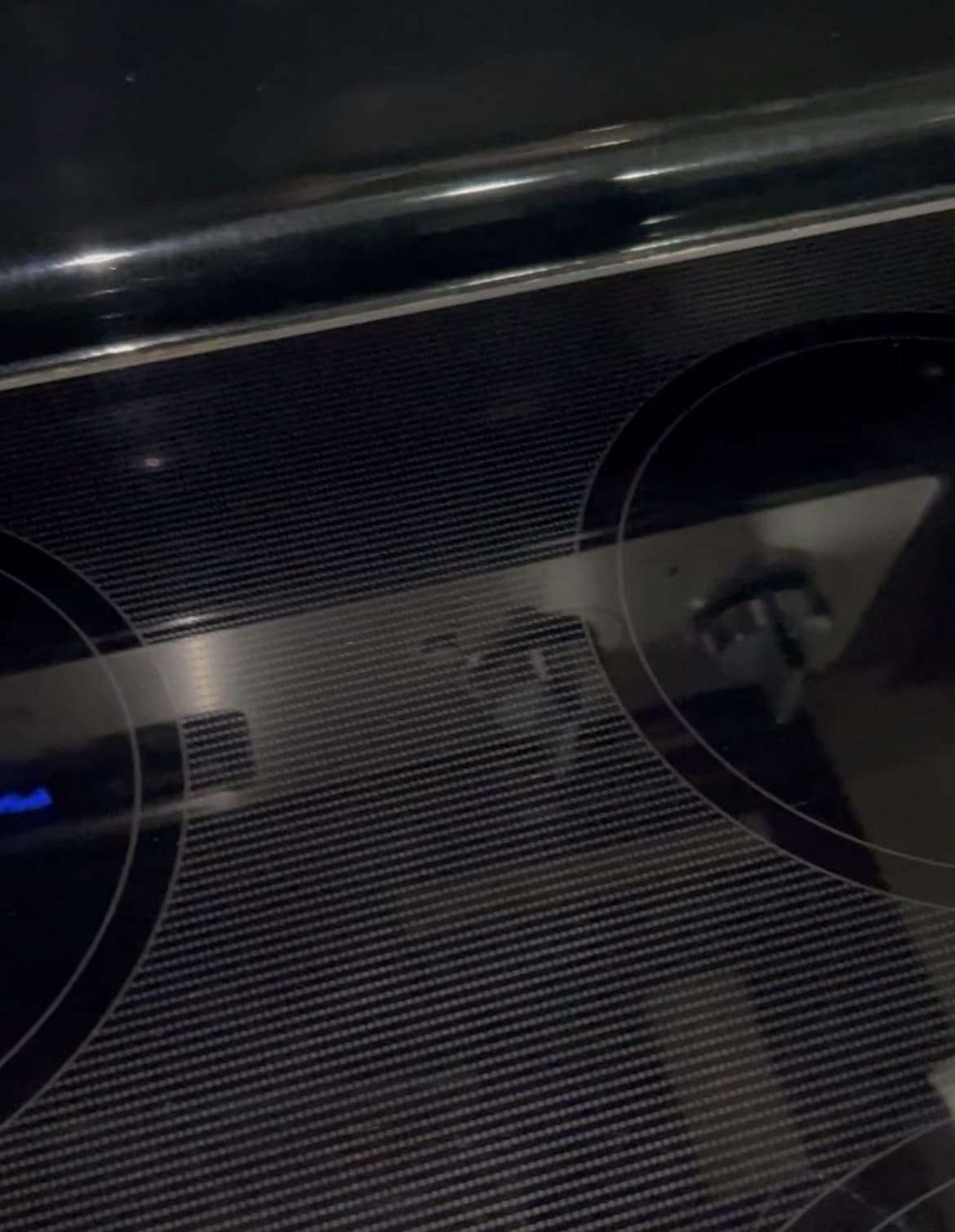 Black glass-top electric stove with circular heating elements and a textured, reflective surface.