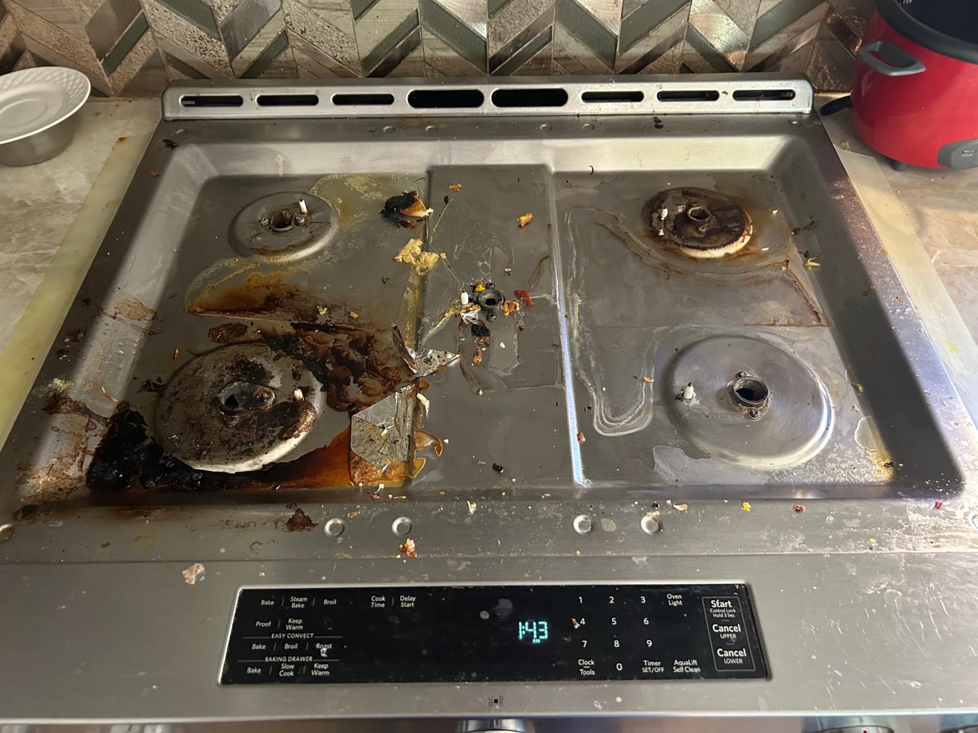 Dirty stainless steel stovetop covered in burnt food, grease, and debris with grates removed.